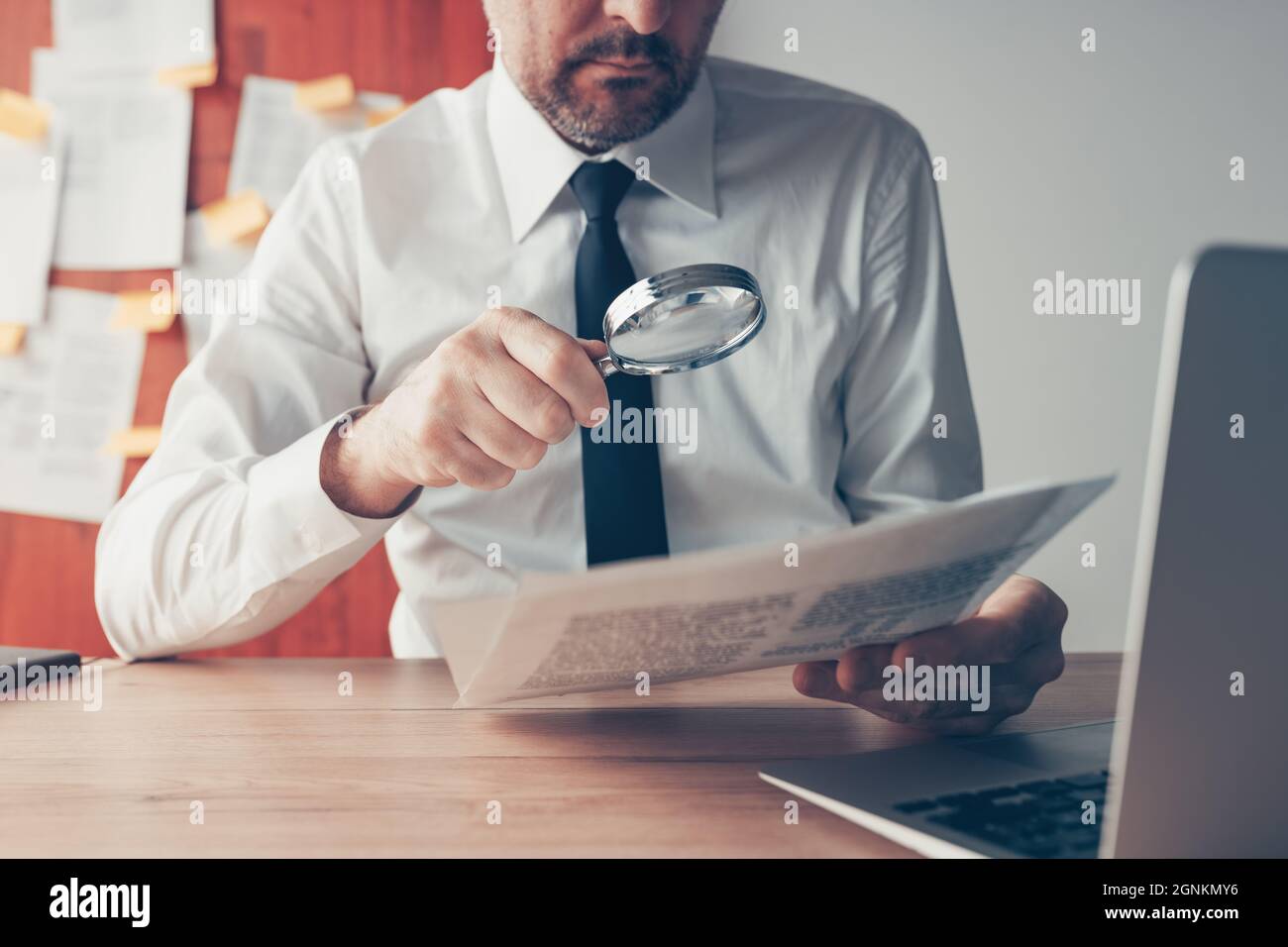 Businessman reading document contract papers with magnifying glass at office desk, close up with selective focus Stock Photo