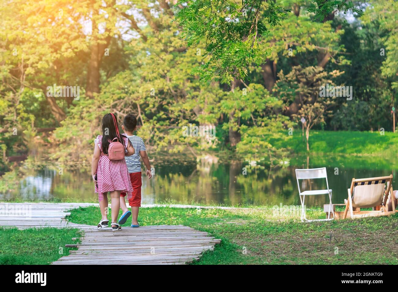 Back view of Asian young girl and boy walking together on pathway ...