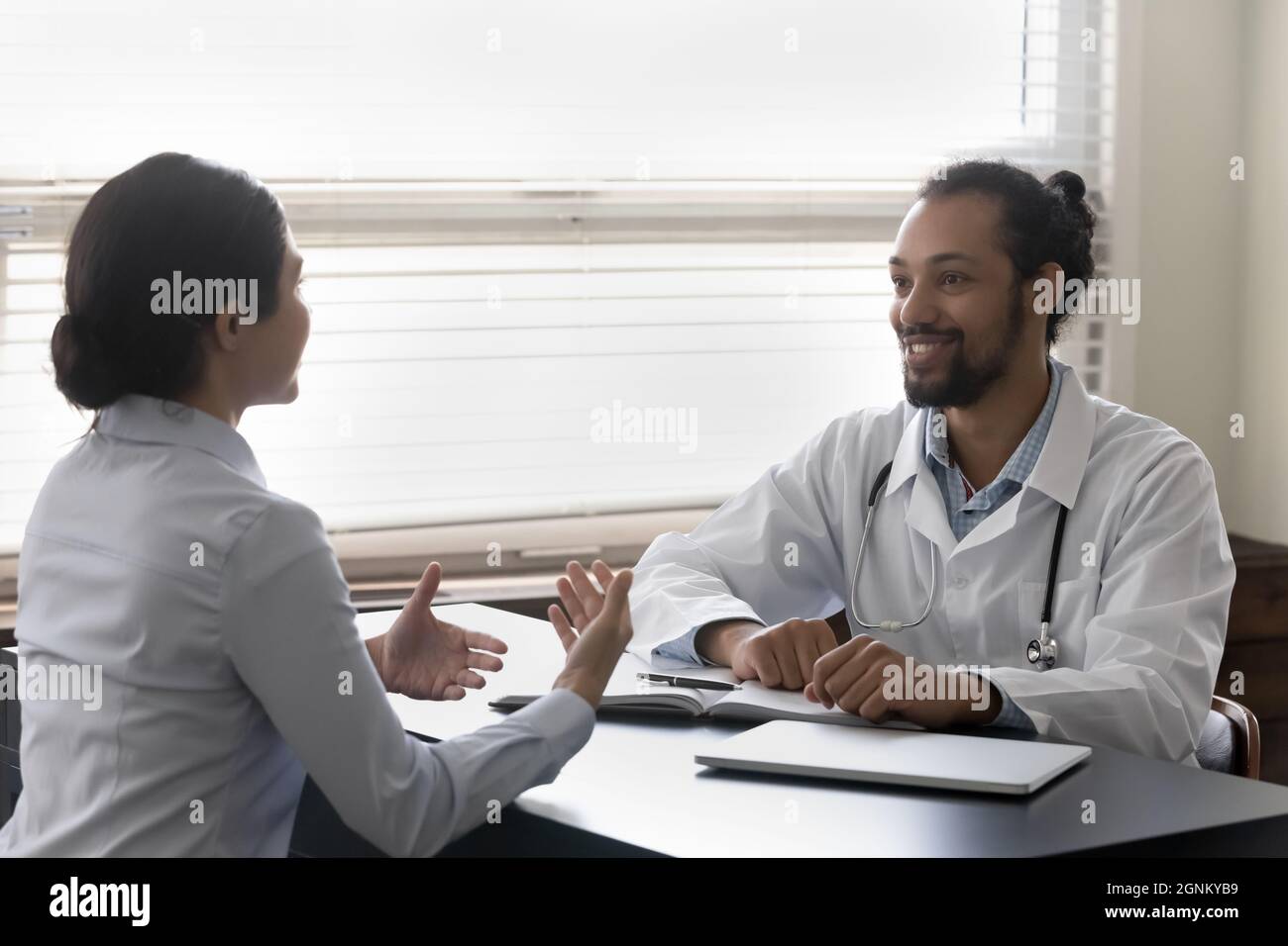 Happy optimistic young doctor listening to patient at appointment Stock Photo