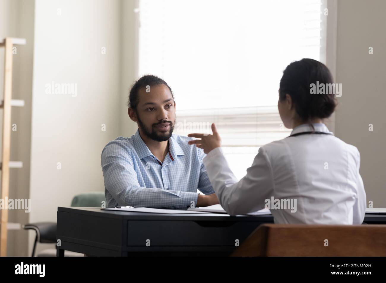 Young male patient visiting doctor, consulting young female general practitioner Stock Photo