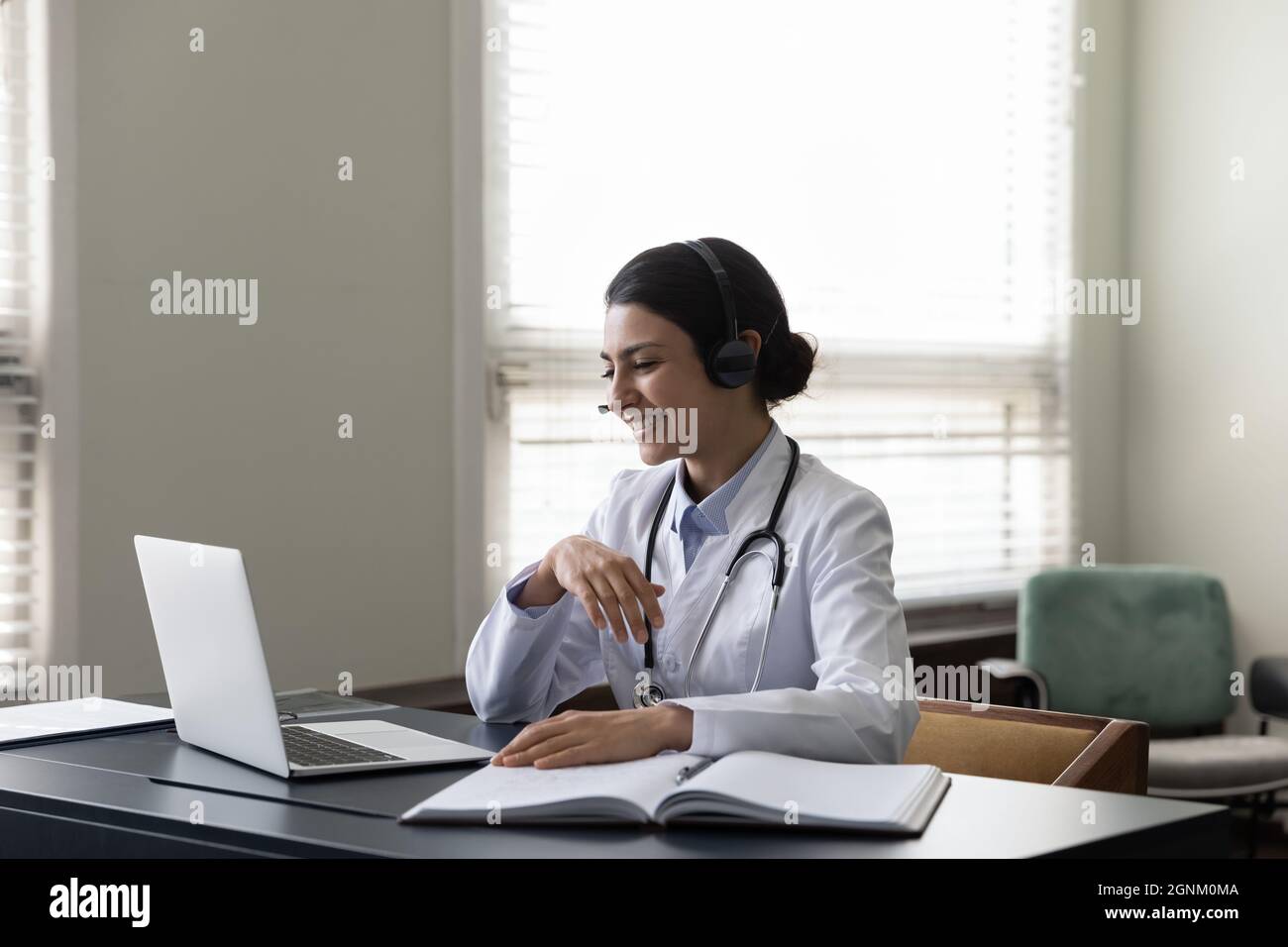 Happy young Indian general practitioner in headphones using laptop Stock Photo