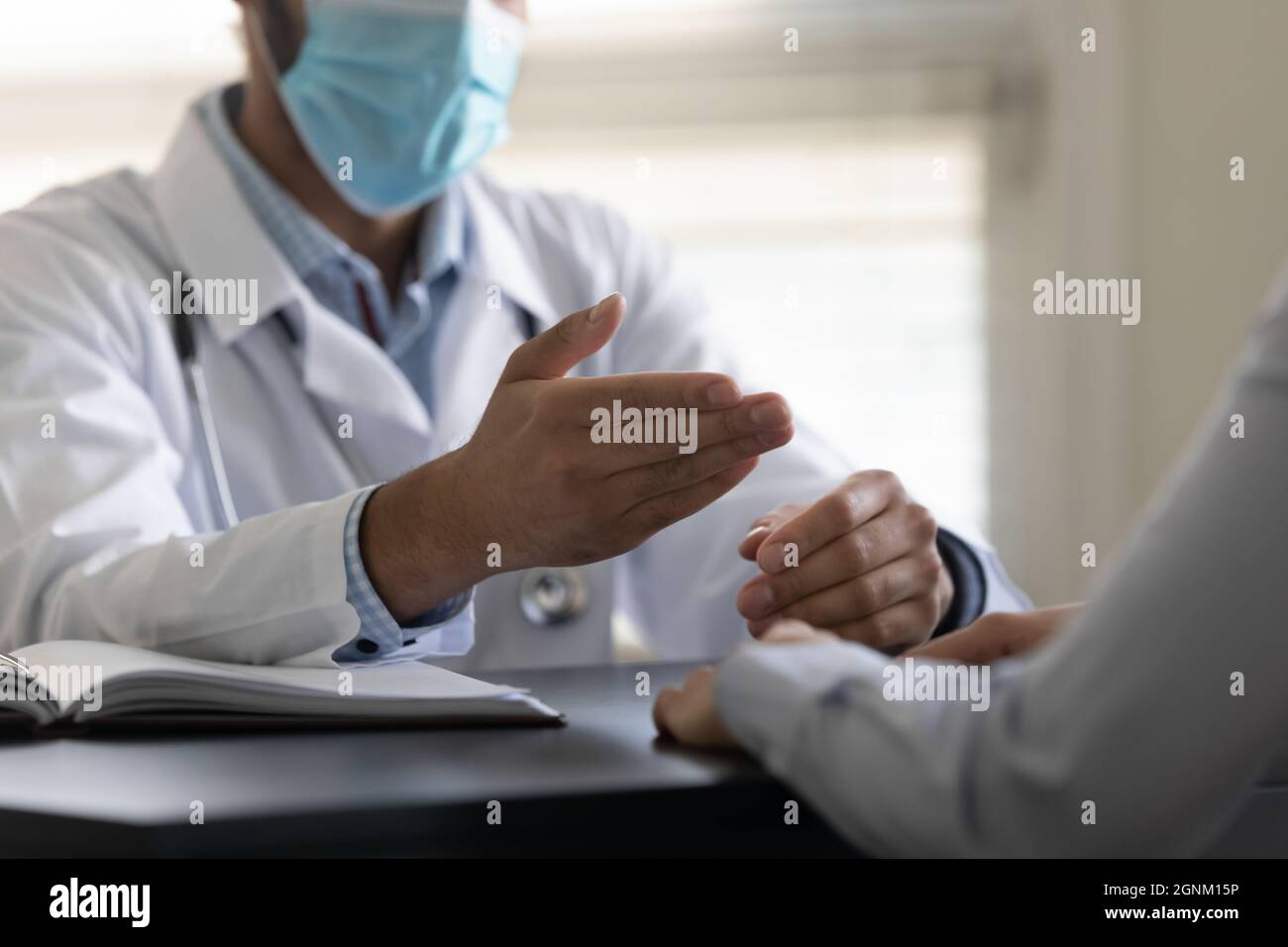 Hands of general practitioner in facemask speaking at appointment Stock Photo
