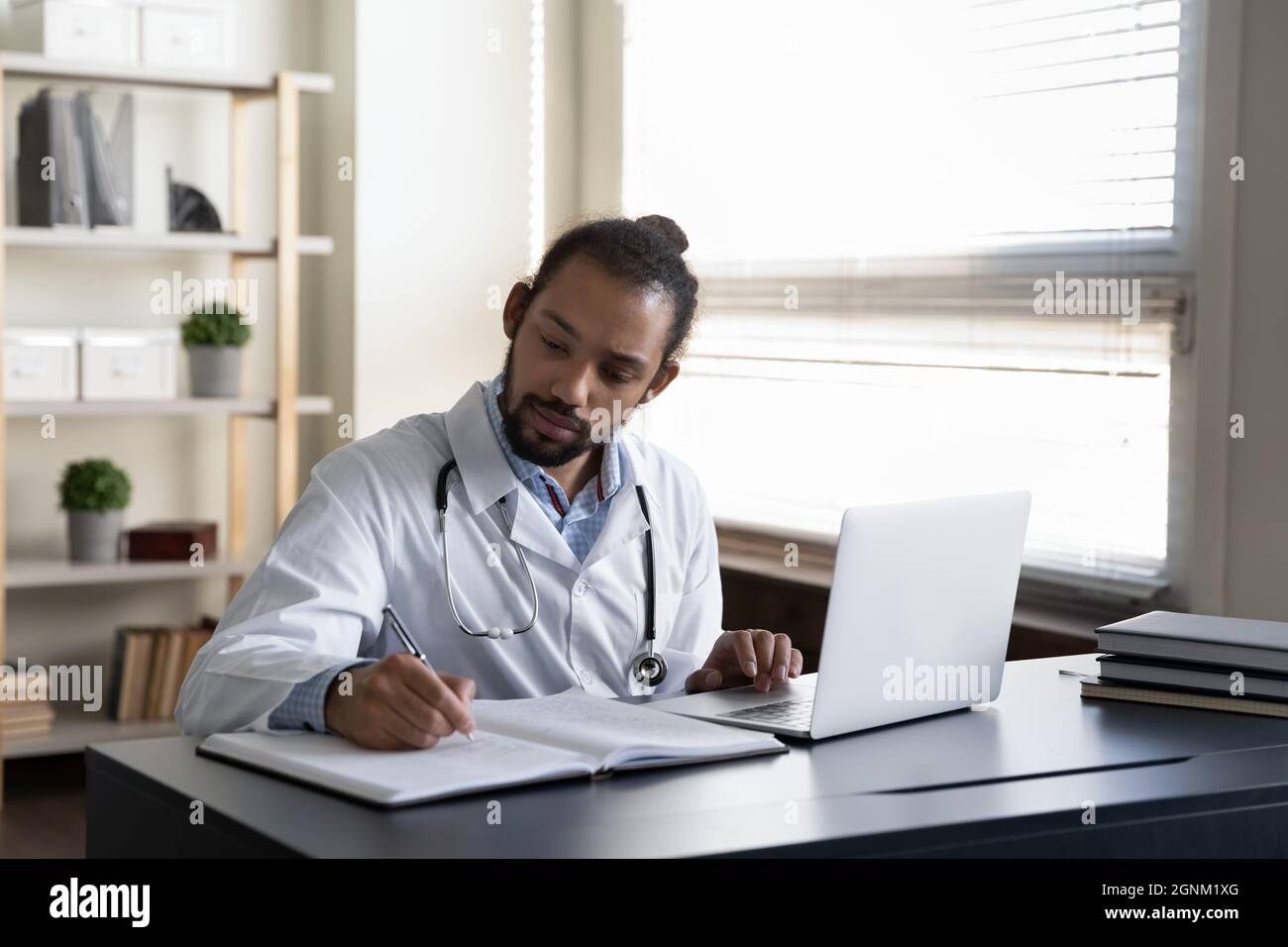 Serious focused GP doctor writing medical records at open laptop Stock