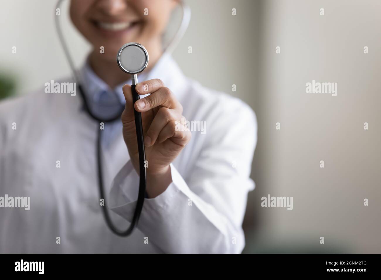 Happy young GP doctor using stethoscope, showing tool at camera Stock Photo