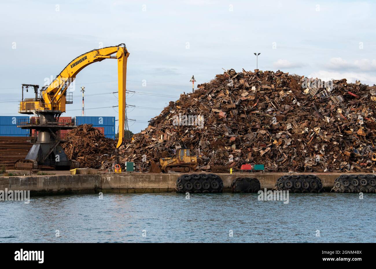 Southampton, England, UK. 2021.  A yellow crawler excavator machine on a dockside moving scrap metal  before loading onto a cargo ship for exporting. Stock Photo