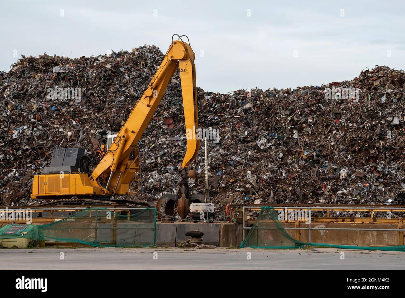 Southampton, England, UK. 2021.  A yellow crawler excavator machine on a dockside moving scrap metal  before loading onto a cargo ship for exporting. Stock Photo