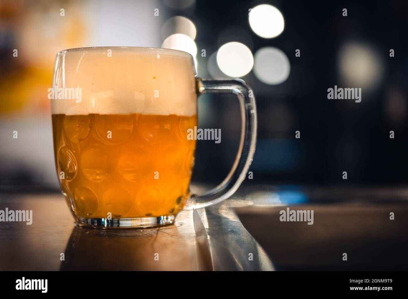 Cold beer glass on a bar or pub desk. Tasty fresh yellow beer of Czech Republic. Dark pub on background. Stock Photo