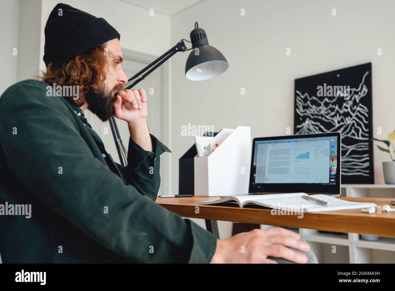 Bearded college student preparing for pass exam at home using laptop. Young man making notes while online learning Stock Photo