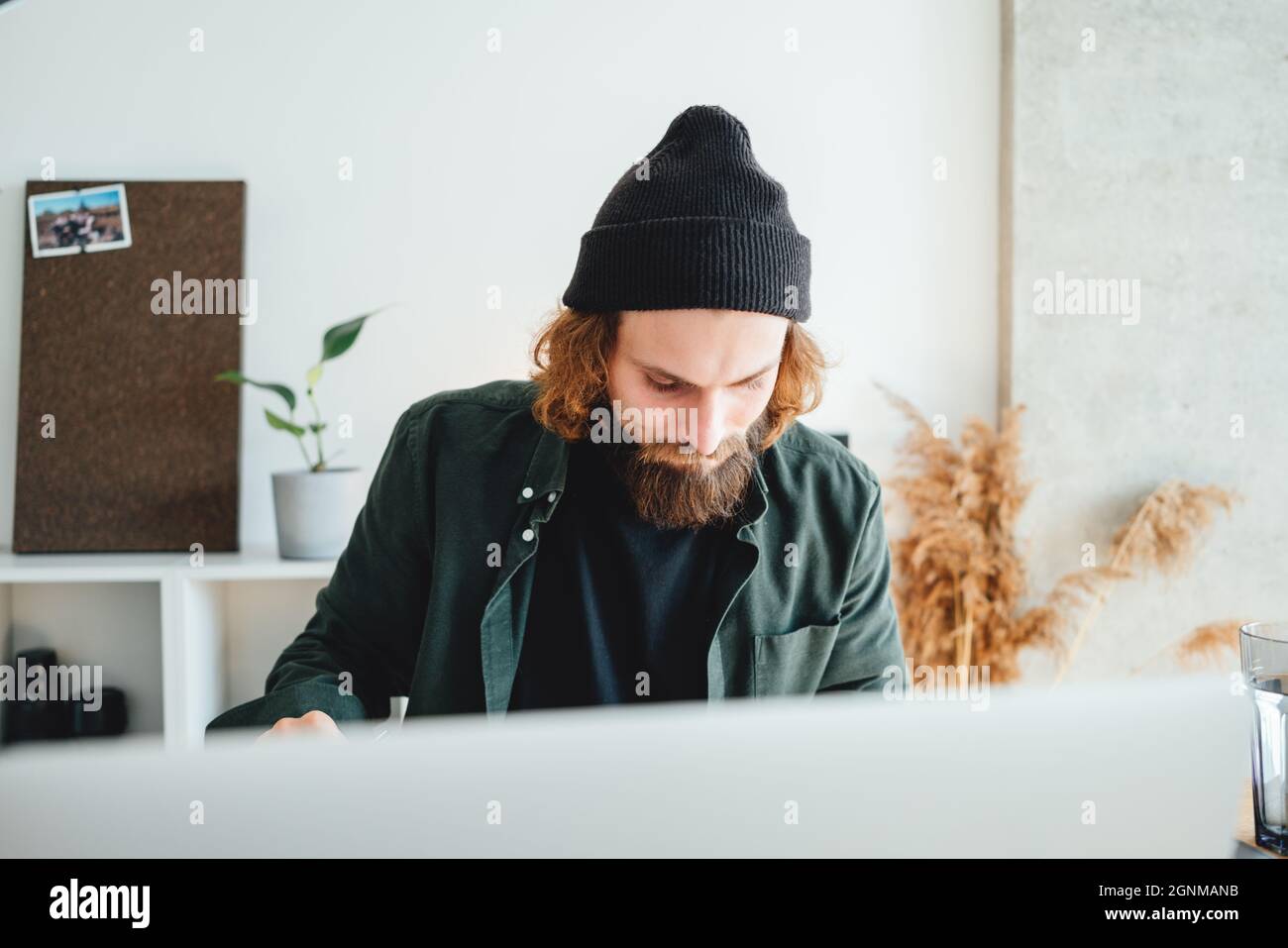 Bearded college student preparing for pass exam at home using laptop. Young man making notes while online learning Stock Photo