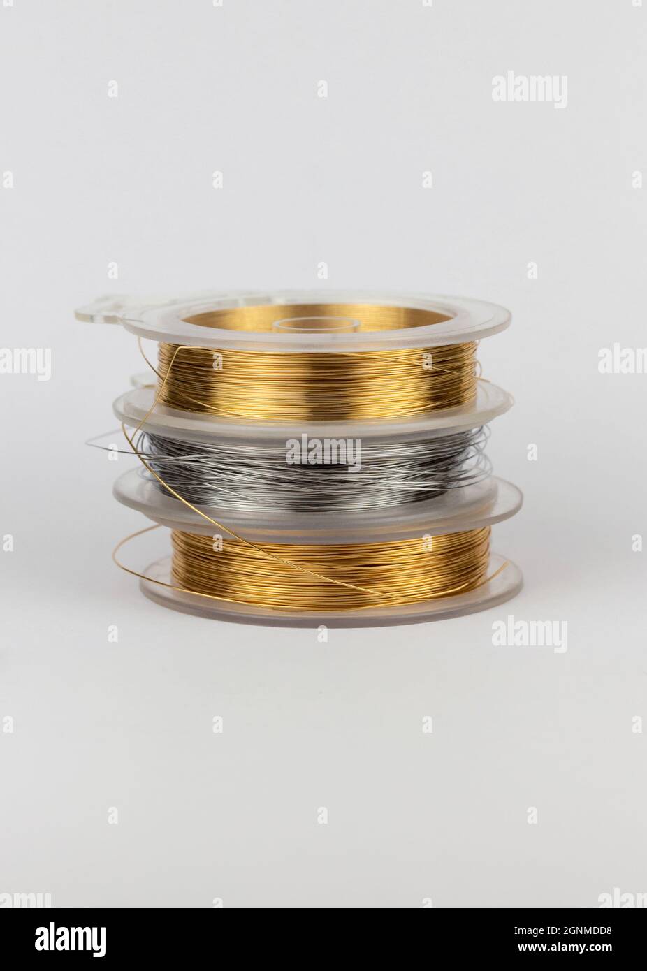 stack of three spools of crafting or jewelry wire in gold, silver and bronze colors on a white background with copy space Stock Photo