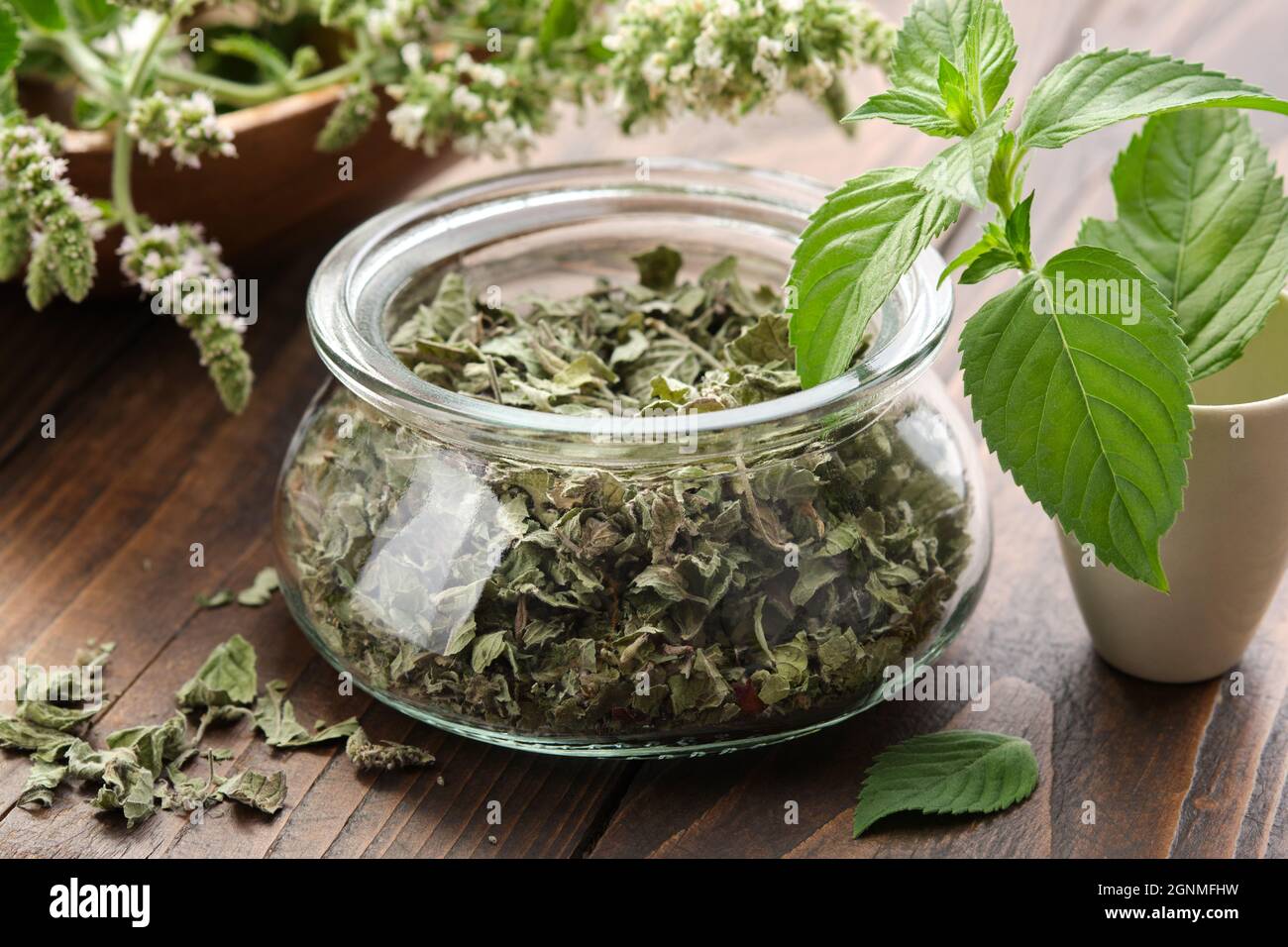 Glass jar of dried mint leaves and blossom peppermint. Mortar of fresh spearmint leaves. Wooden bowl of blossom Mentha piperita medicinal plants on ba Stock Photo