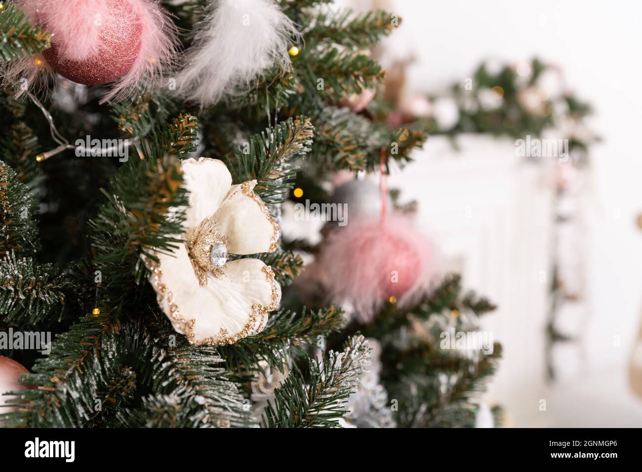 Christmas decorated tree in soft pink colors against the background of white classic fireplace with Christmas decorations. Details of New Year festive Stock Photo