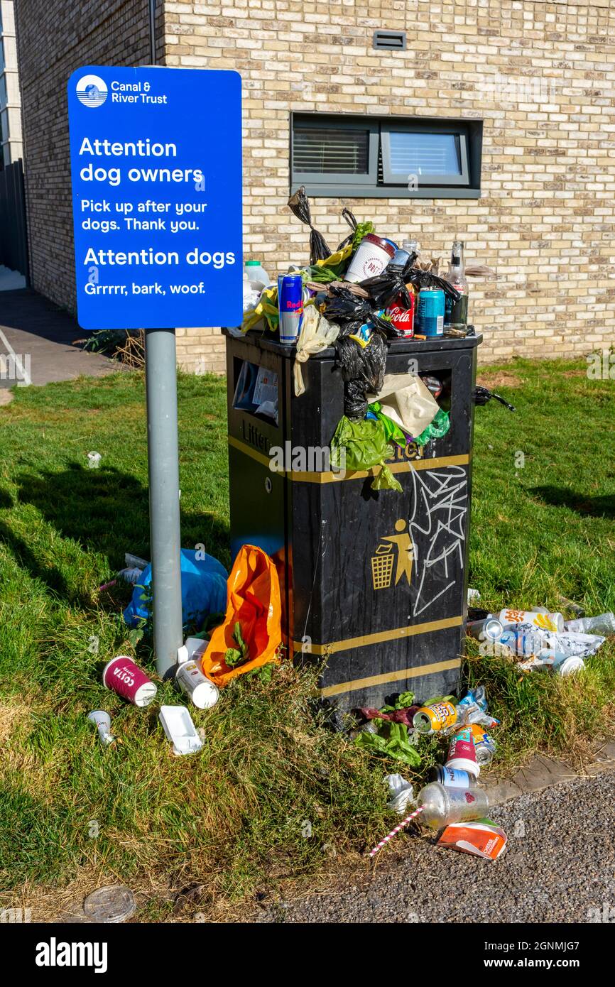 Sign asking dog owners to pick up after their dogs, next to a packed and overflowing waste bin.  By the Ashton Canal, Ancoats, Manchester, England, UK Stock Photo