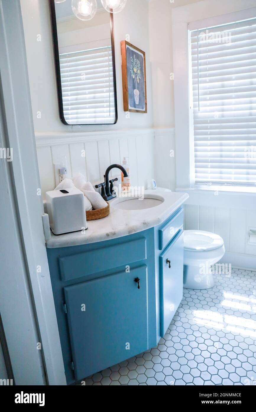 A small guest bathroom with a vintage blue vanity, retro black mirror, and clear glass light fixture in a recently renovated short term rental cottage Stock Photo
