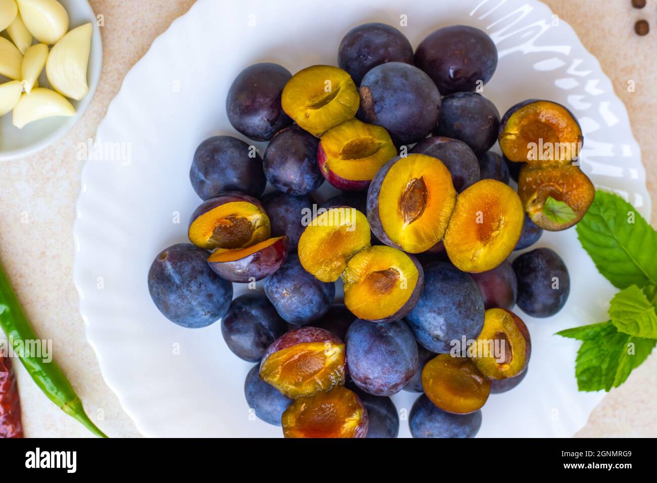 Cooking spicy plum sauce. Ingredients for tkemali on the table plate with plums, seasonings, close-up. Stock Photo