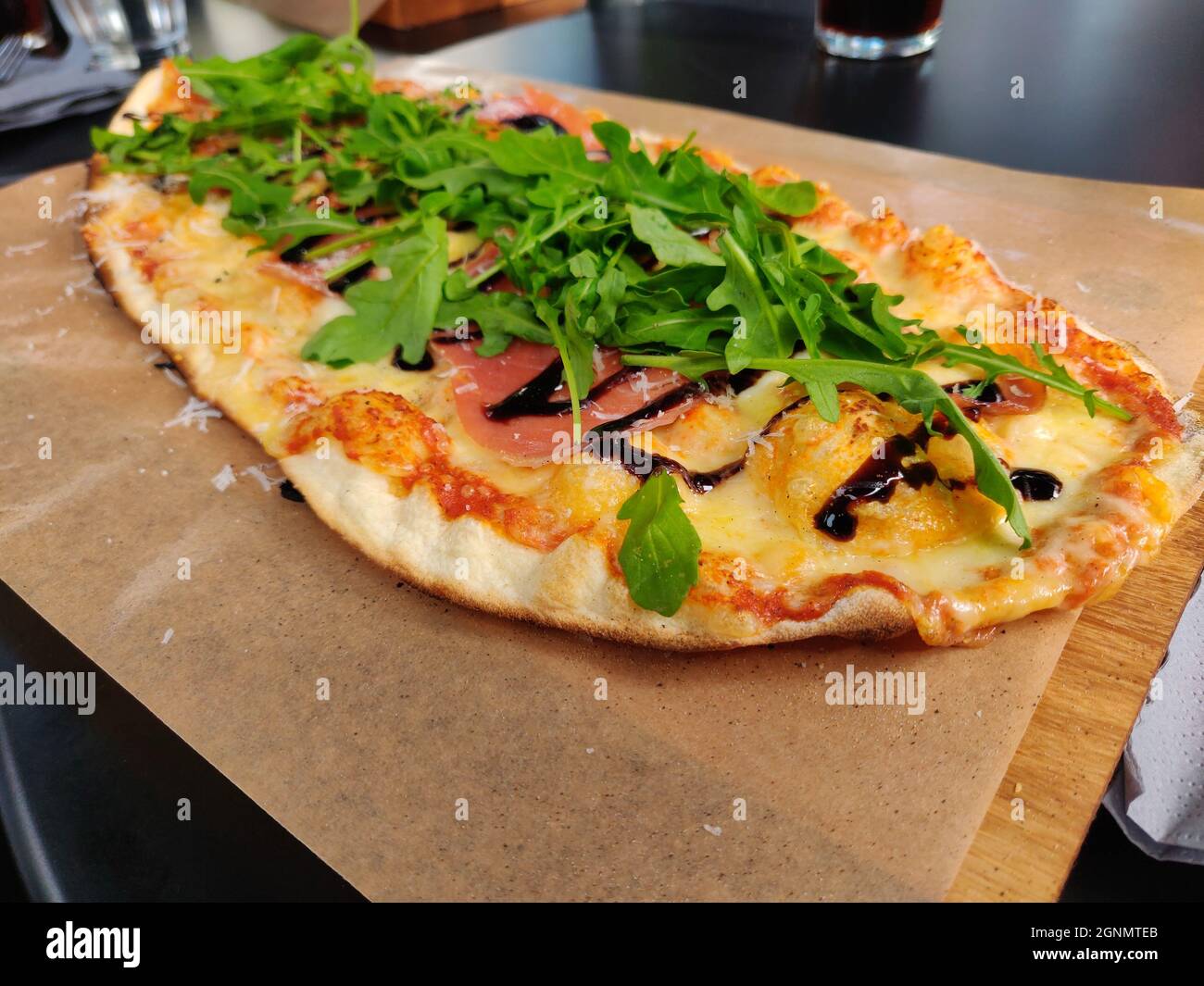 A close-up shot of an oval-shaped delicious freshly baked pizza with cheese, bacon ham, and arugula Stock Photo