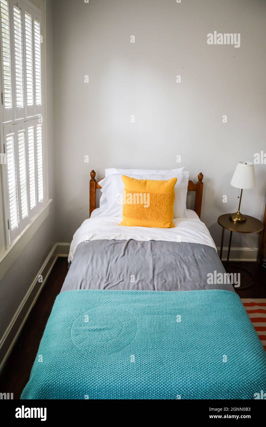 A guest bedroom with a single twin bed with turquoise and gray bedspread and yellow decorative pillow Stock Photo