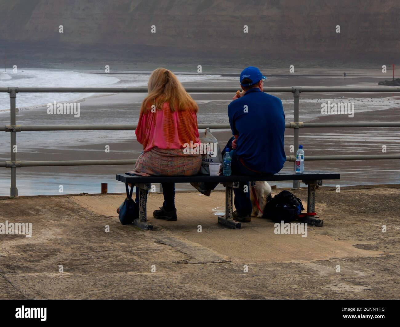 Man a woman and a  dog enjoyng a picnic on a bench overlooking the sea at Skinningrove Stock Photo