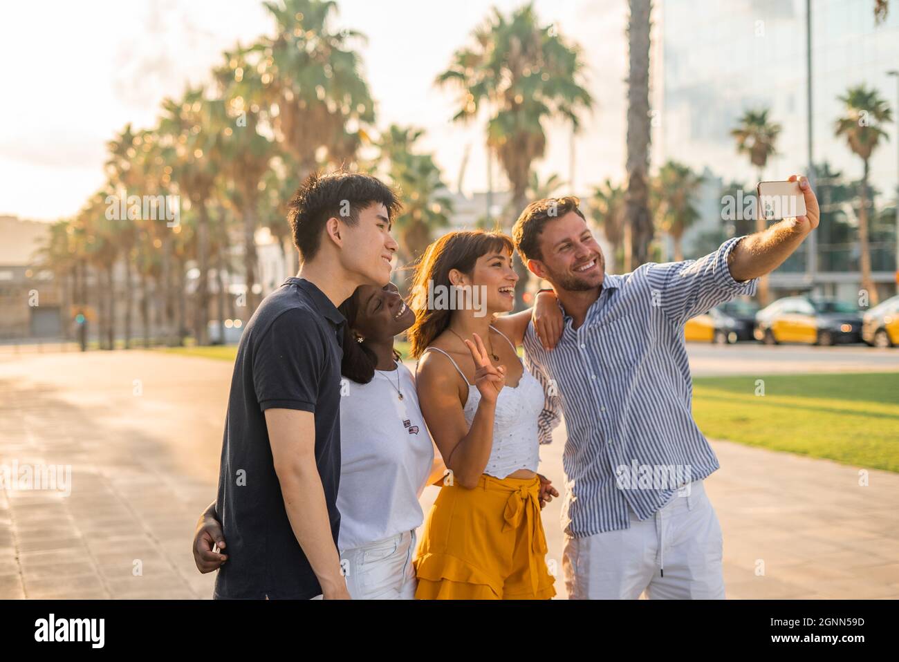 Group of cheerful young multiracial friends in casual clothes taking selfie on smartphone while standing on street and enjoying summer day together Stock Photo