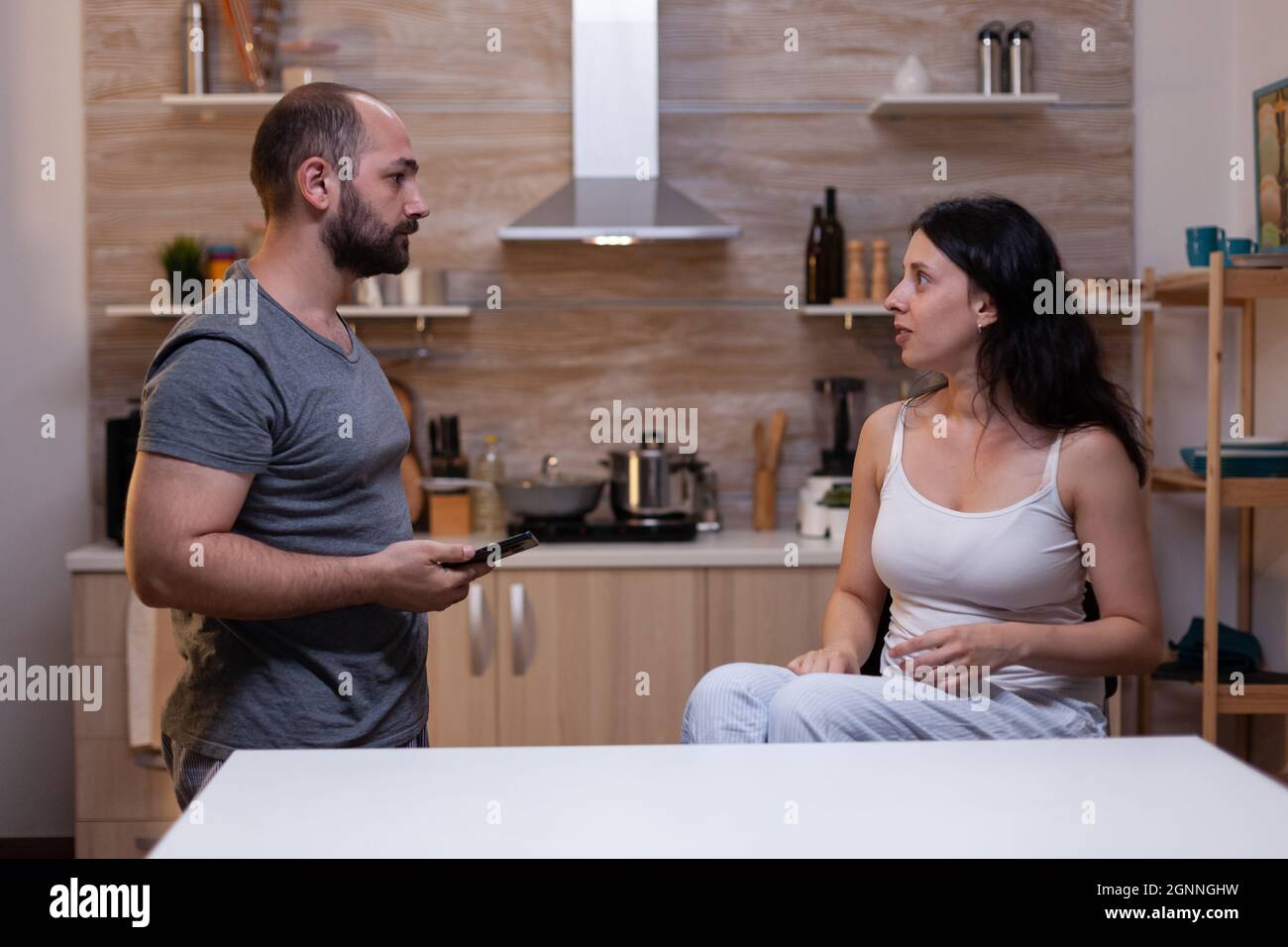 Upset wife caught cheating by jealous husband holding smartphone for text messages proof. Angry man fighting with woman about infidelity and secret boyfriend. Relationship crisis Stock Photo