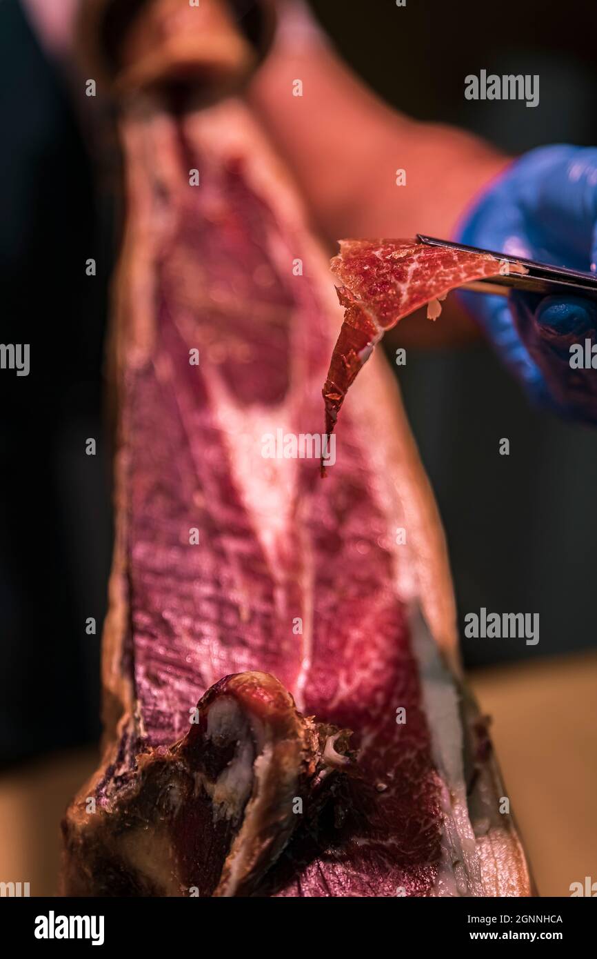 Whole bone-in leg of Spanish serrano iberico ham being carved at a local butcher shop in the old town or Casco Viejo in Pamplona, Spain Spain Stock Photo
