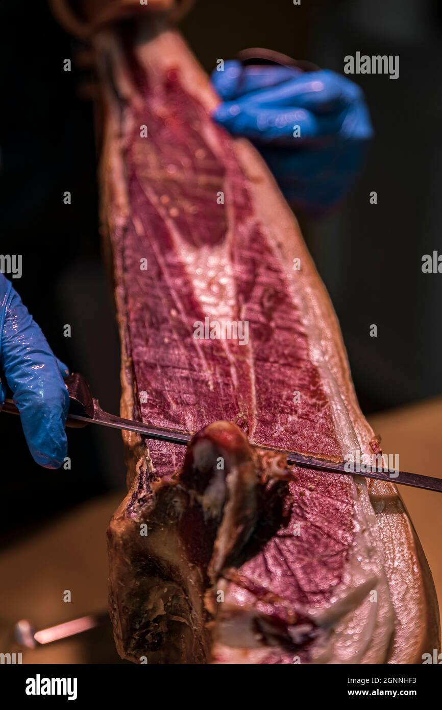Whole bone-in leg of Spanish serrano iberico ham being carved at a local butcher shop in the old town or Casco Viejo in Pamplona, Spain Stock Photo