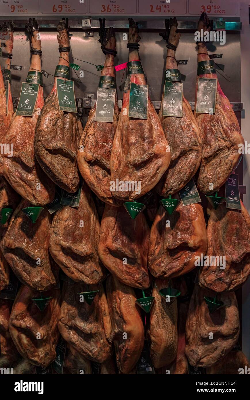 Multiple whole bone-in legs of Spanish serrano iberico ham hanging on display at a butcher shop in the old town or Casco Viejo in Pamplona, Spain Stock Photo