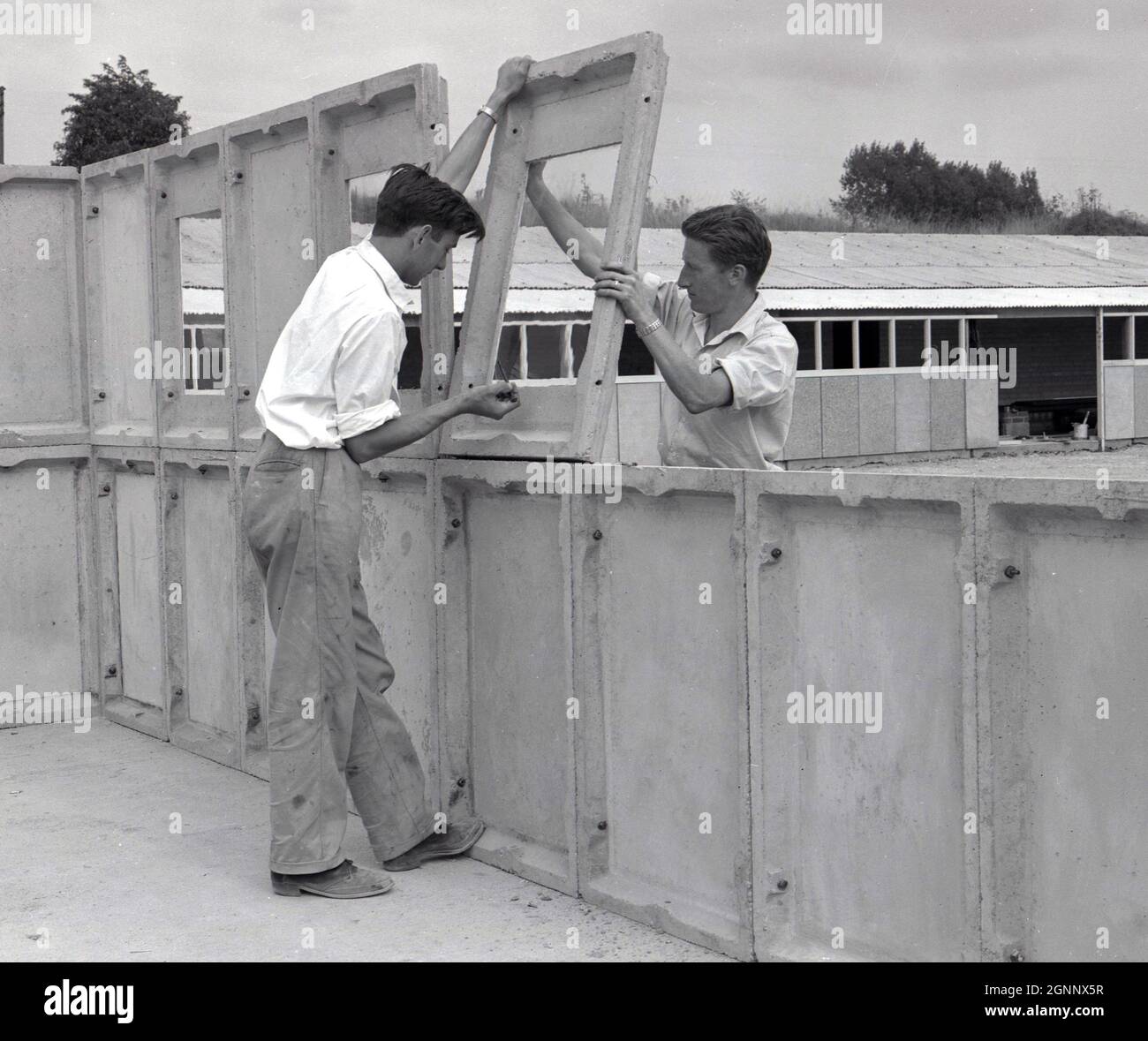 1960s, historical, constructing a prefab garage on an industrial premises at Witney, Oxford, England, UK, for demonstration purposes, Two workers fixing or bolting the upper level precast concrete panels in position. Stock Photo