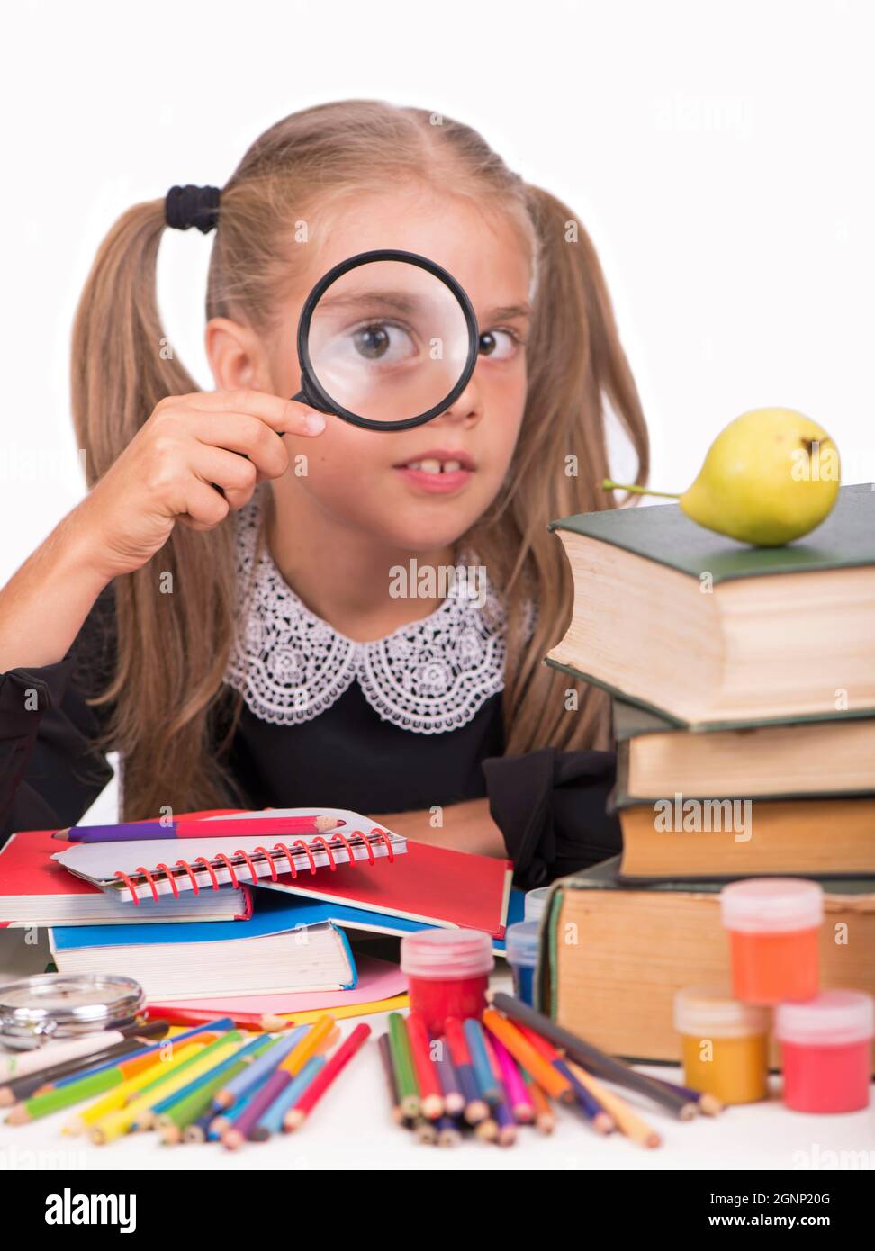 Little girl, blonde in a school dress looks through a magnifying glass on a white background Stock Photo