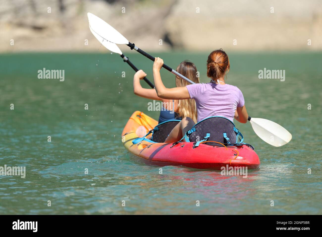 Back view portrait of two women rowing in a tandem kayak in a lake Stock Photo