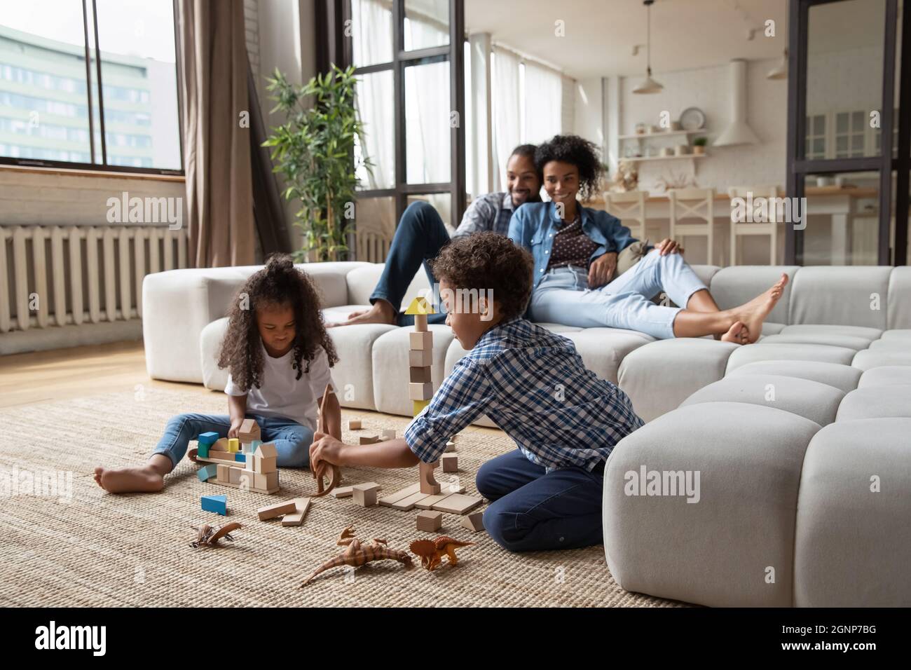 Little African American kids playing while parents relaxing on couch