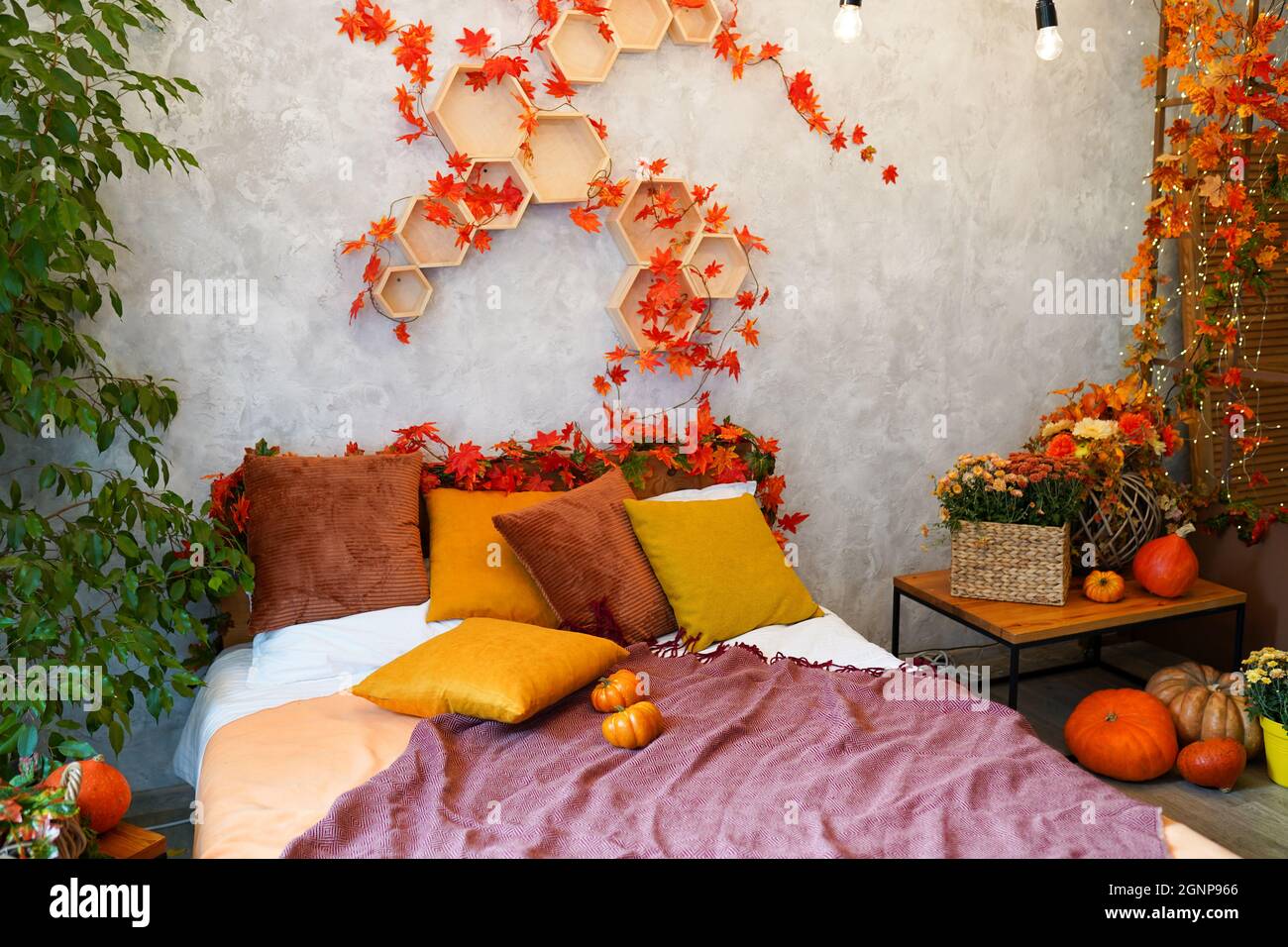 Home autumn decor. Cozy fall bedroom interior bed with orange pillows, flowers, pumpkins, Autumn decoration. Stock Photo