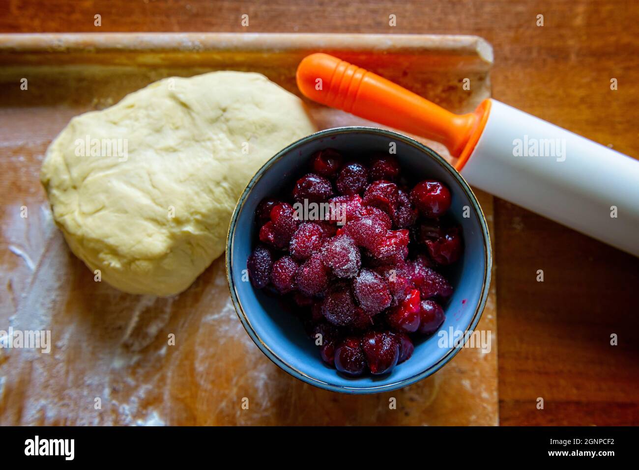 Making dumplings filled with sour cherry with sugar on a wooden cutting board, or cherru cake Stock Photo