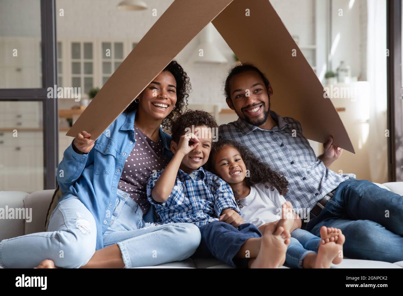 Happy African American family sitting on couch under cardboard roof Stock Photo