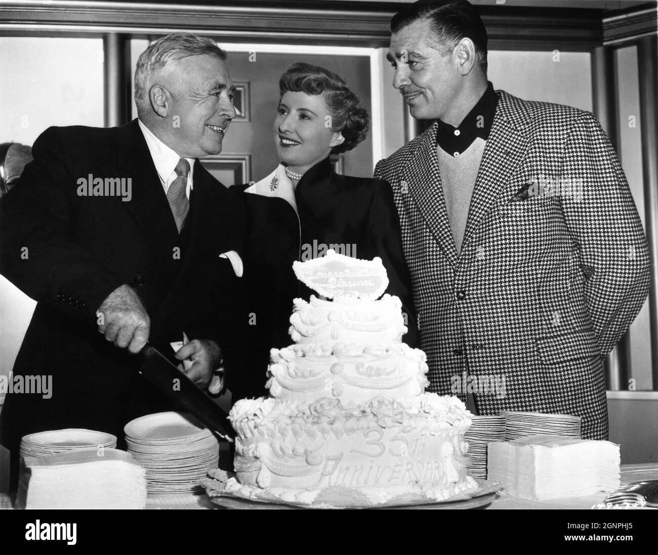 Director CLARENCE BROWN cuts cake celebrating his 35th Anniversary in motion pictures with CLARK GABLE and BARBARA STANWYCK on set candid during filming of TO PLEASE A LADY 1950 director CLARENCE BROWN story / screenplay Barré Lyndon and Marge Decker costume design Helen Rose Metro Goldwyn Mayer Stock Photo