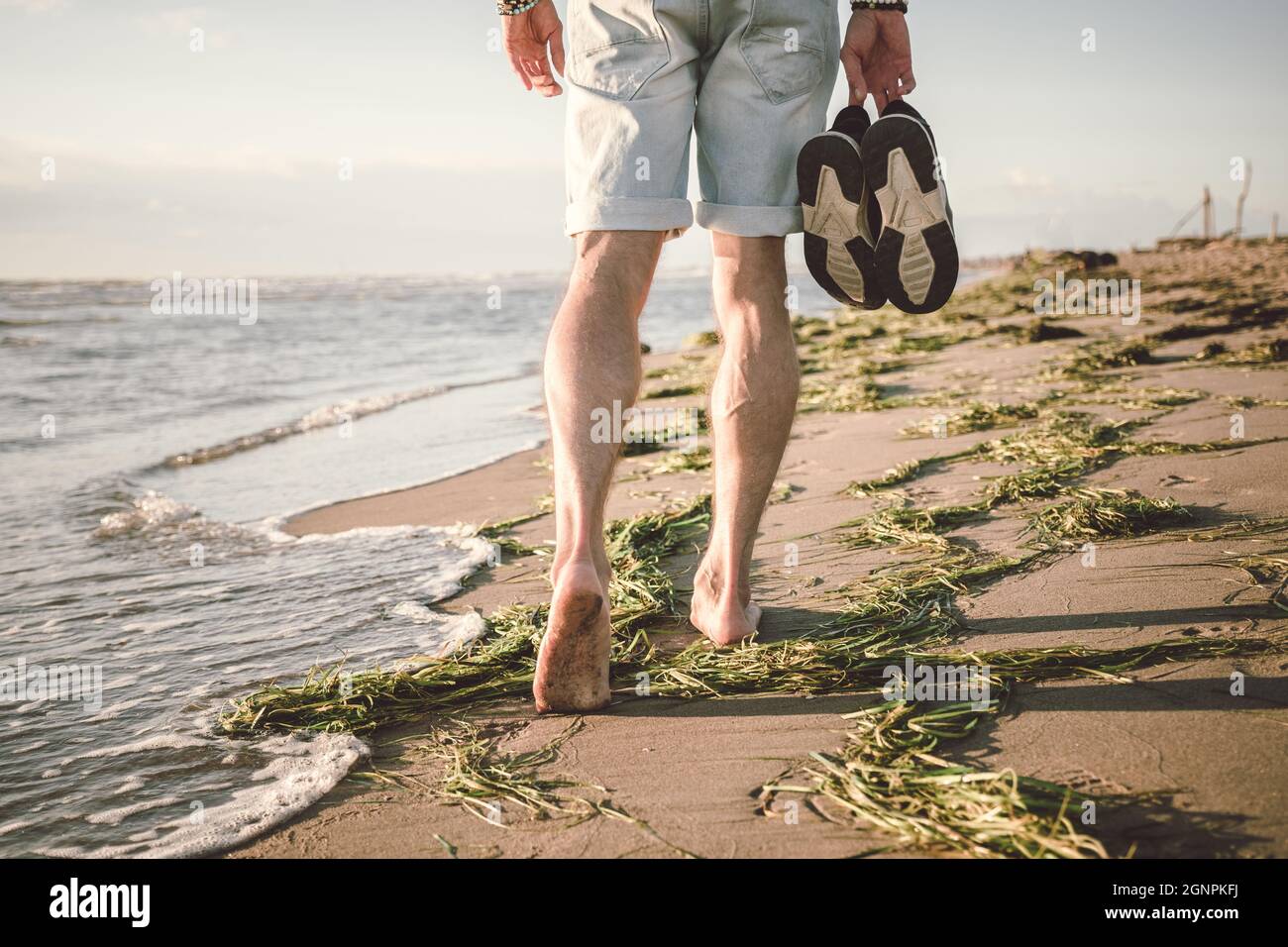 Young man walking barefoot on the beach in sunset time. Nature and travel concept Stock Photo