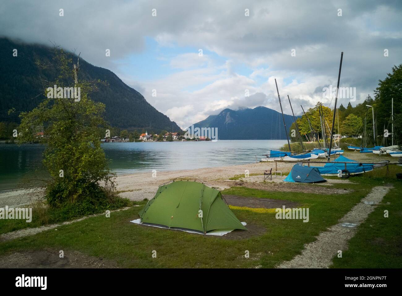 Small green tent and boats next to beach on campground camping Walchensee in the alpine upland with lake and mountain Herzogstand in background Stock Photo