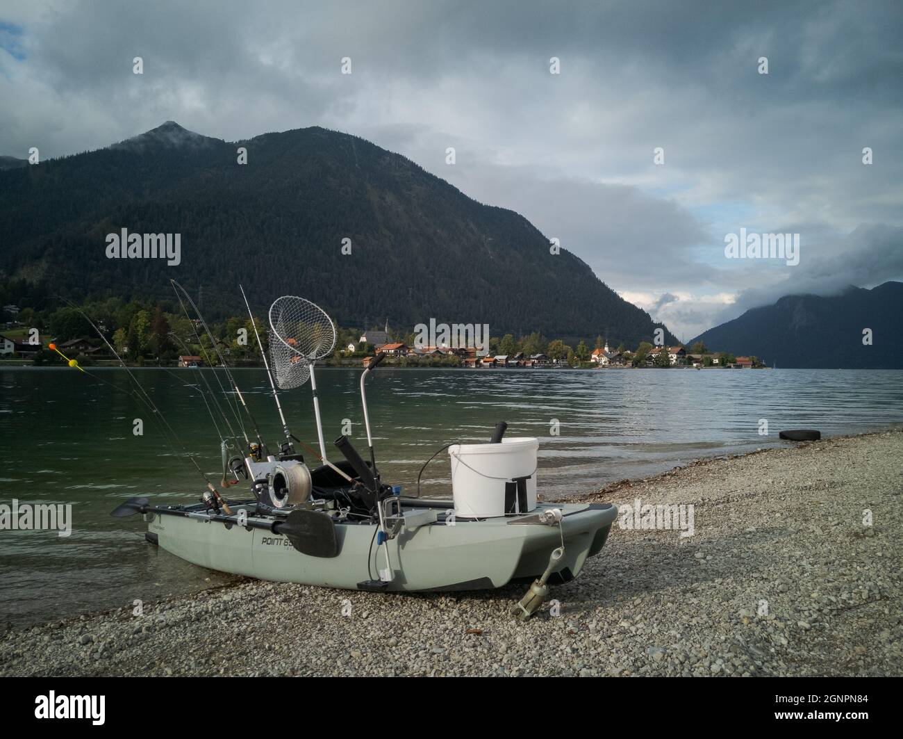 Fancy fishing boat on the beach with fishing rods, brailer and bucket on campground camping Walchensee in the alpine upland with lake and mountain Her Stock Photo