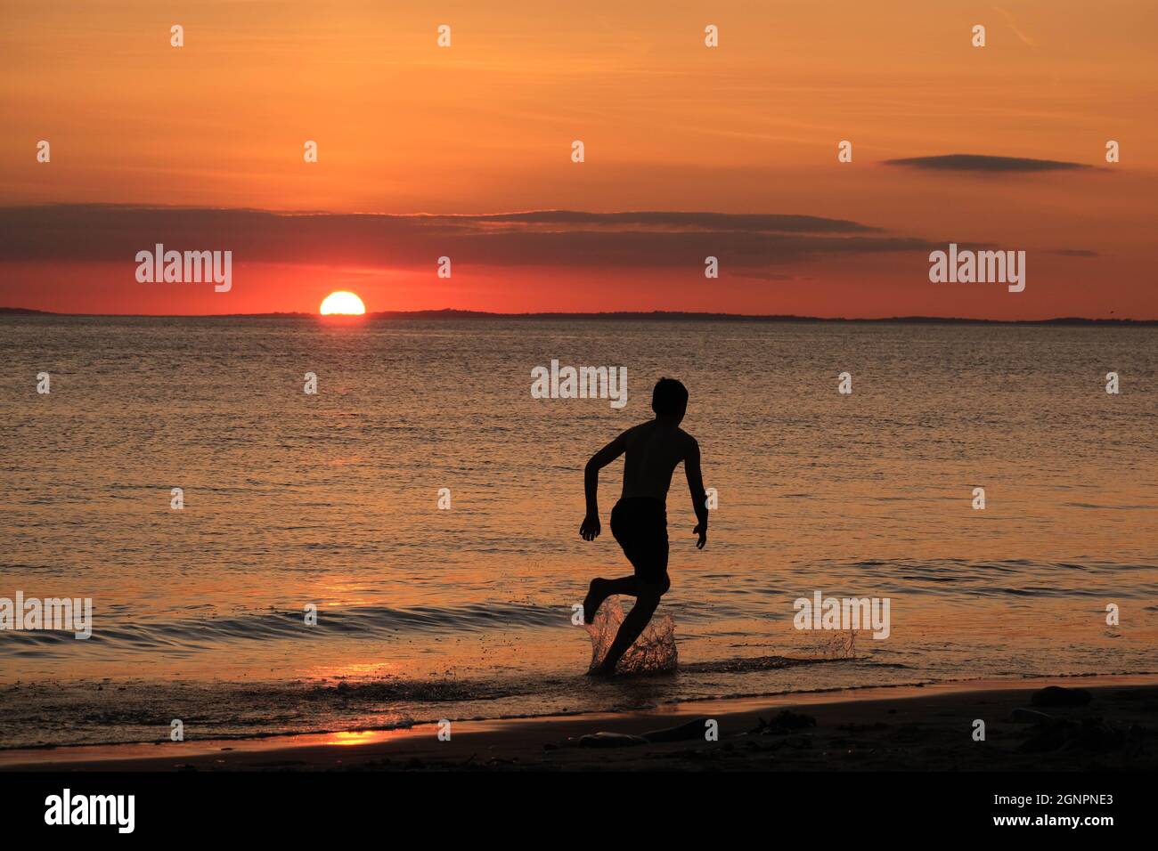Gower, Swansea, UK. 24th August 2021.  UK weather:  A boy enjoys skim boarding the shallows under a setting sun on a dry, fine  and sunny evening at Llangennith beach on the Gower peninsula. The outlook for the next few days is for similarly fine weather with some warm spells.Credit: Gareth Llewelyn/Alamy Stock Photo