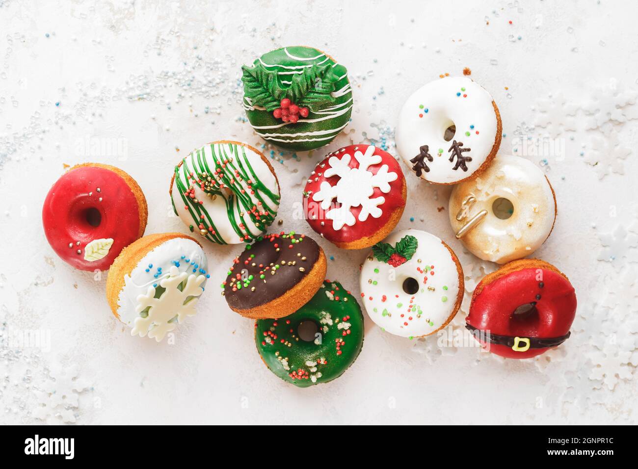 Homemade Glazed Christmas Donuts. Assorted homemade glazed donuts with sprinkles on white festive background. Top view, blank space Stock Photo