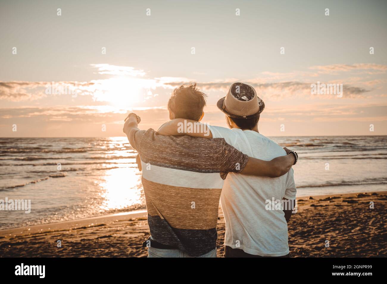 Two friends hug each other looking sunset on the beach. Friendship and love concept Stock Photo