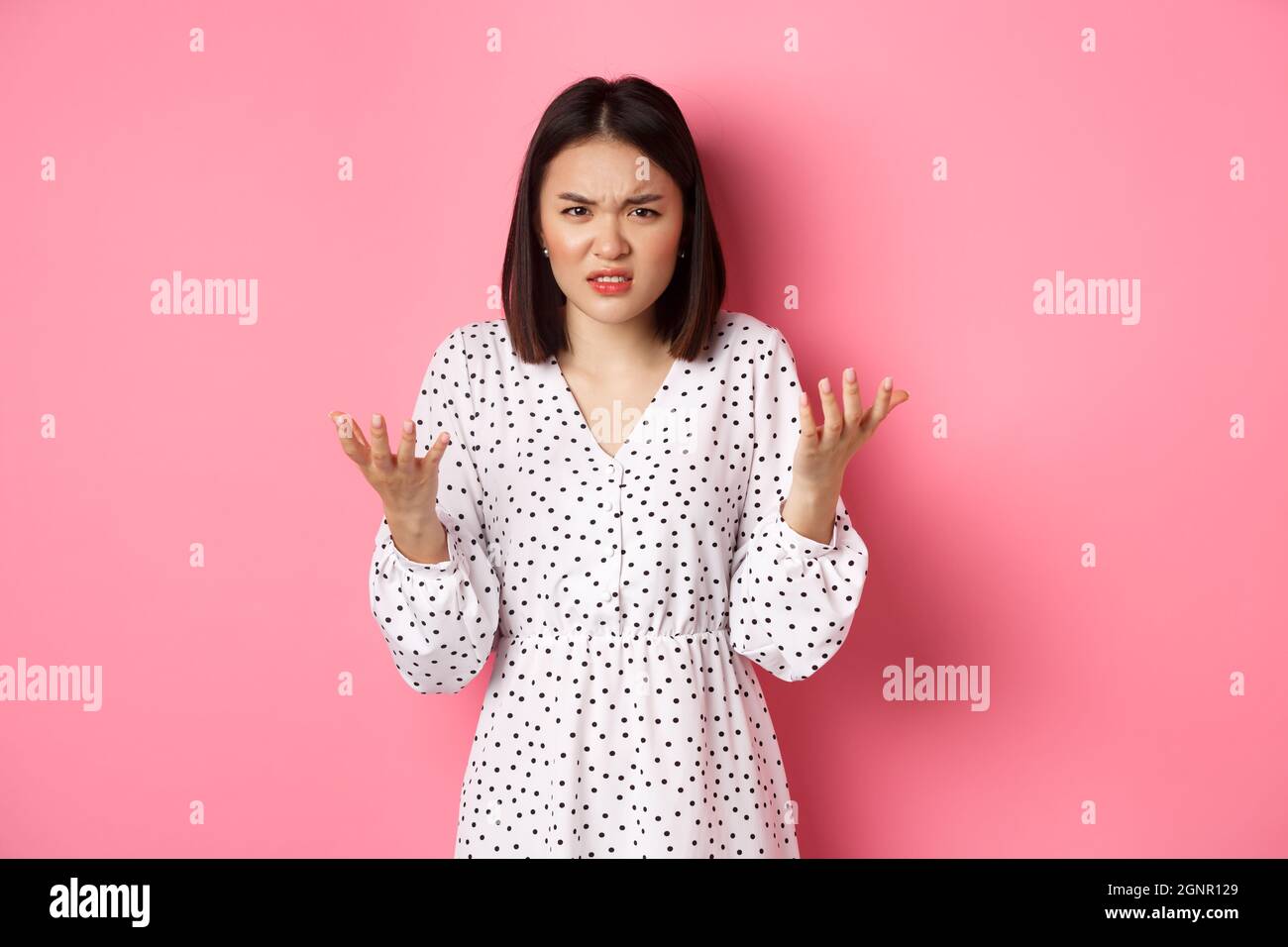 Angry and confused asian woman pointing hands at camera and grimacing ...