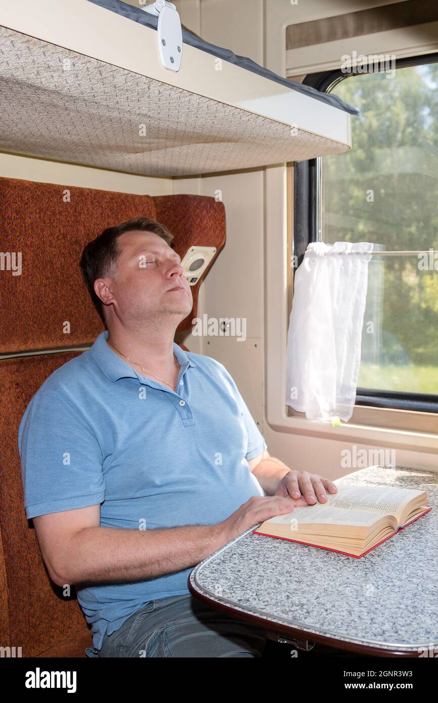 A man fell asleep while reading book in his compartment car, got seasick on train. Stock Photo