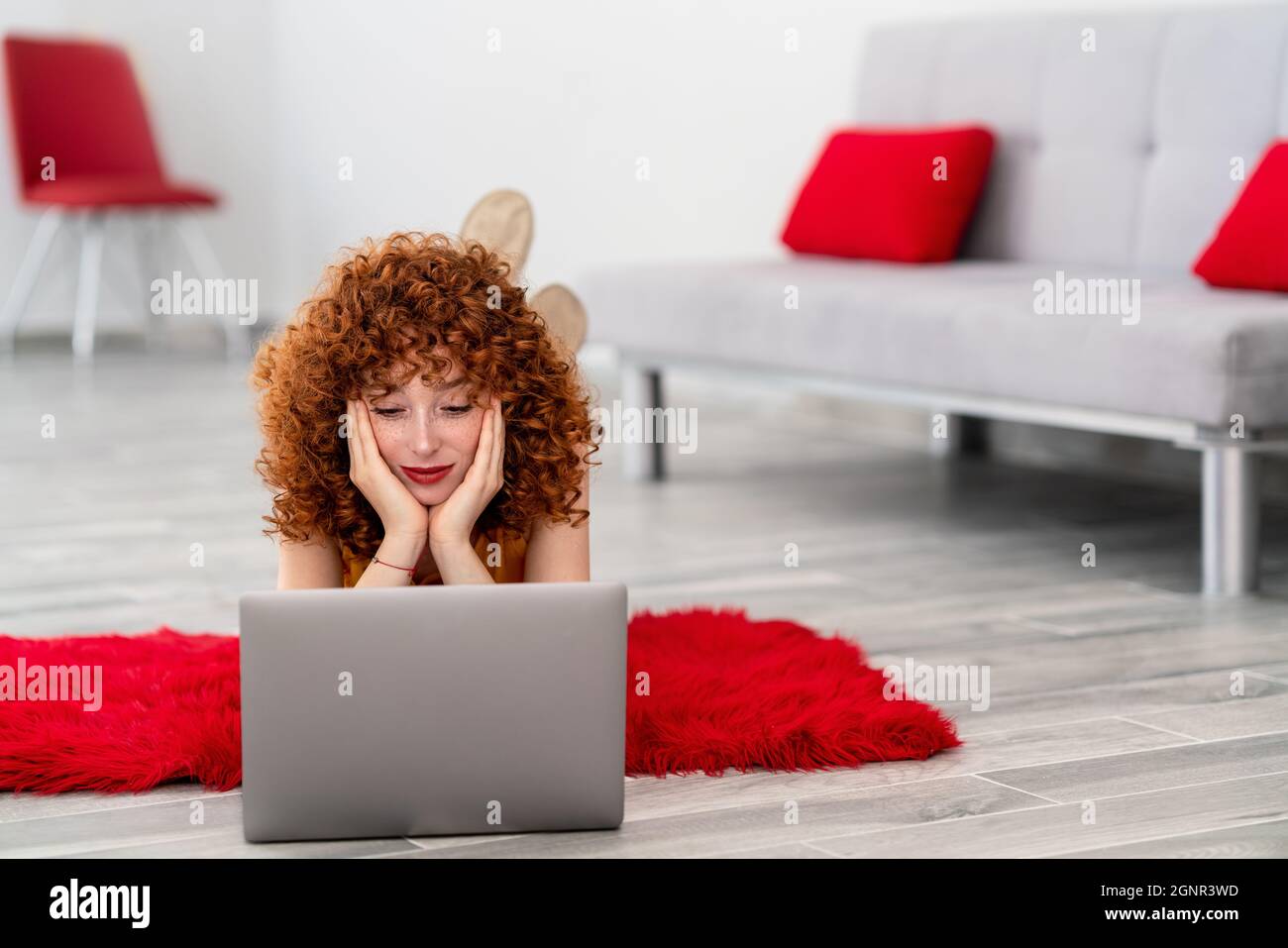 Young woman laying on a red pluffy carpet and using her laptop. High quality photo Stock Photo