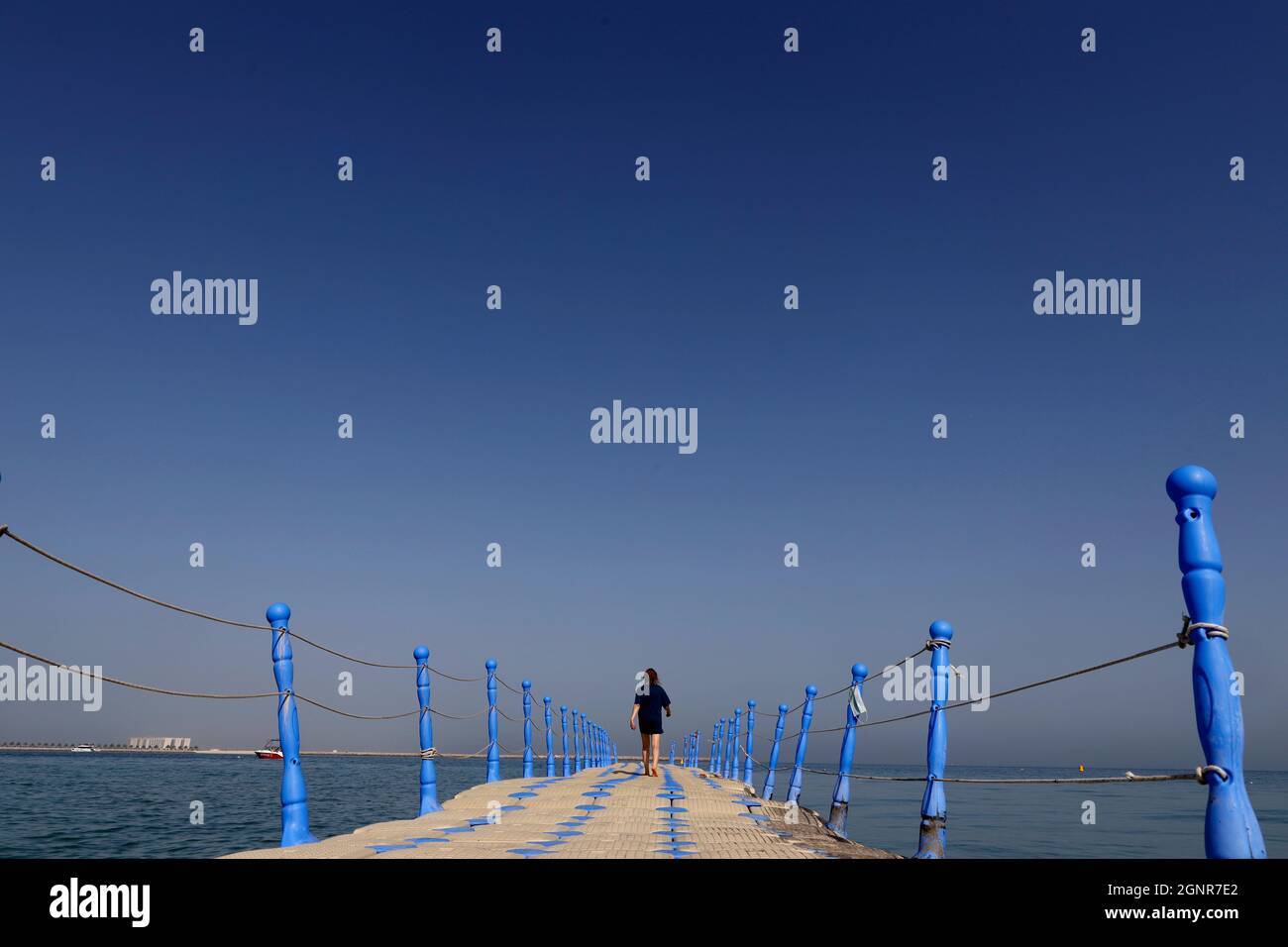 Woman  walking on plastic pontoon walk way floating in the sea.  Al Hamra Beach on the Arabian Gulf at Ras Al Khaimah. United Arab Emirates. Stock Photo