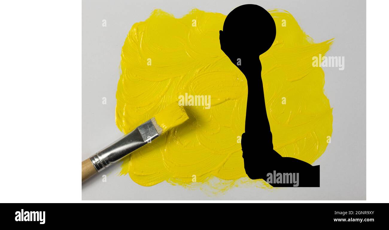 Silhouette of hand holding a ball against yellow paint stain and brush on white background Stock Photo