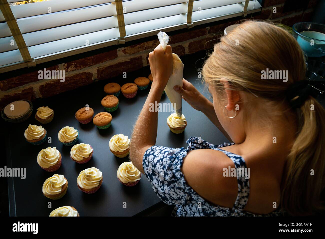 child is decorating her freshly baked cupcakes in the kitchen with butter cream Stock Photo