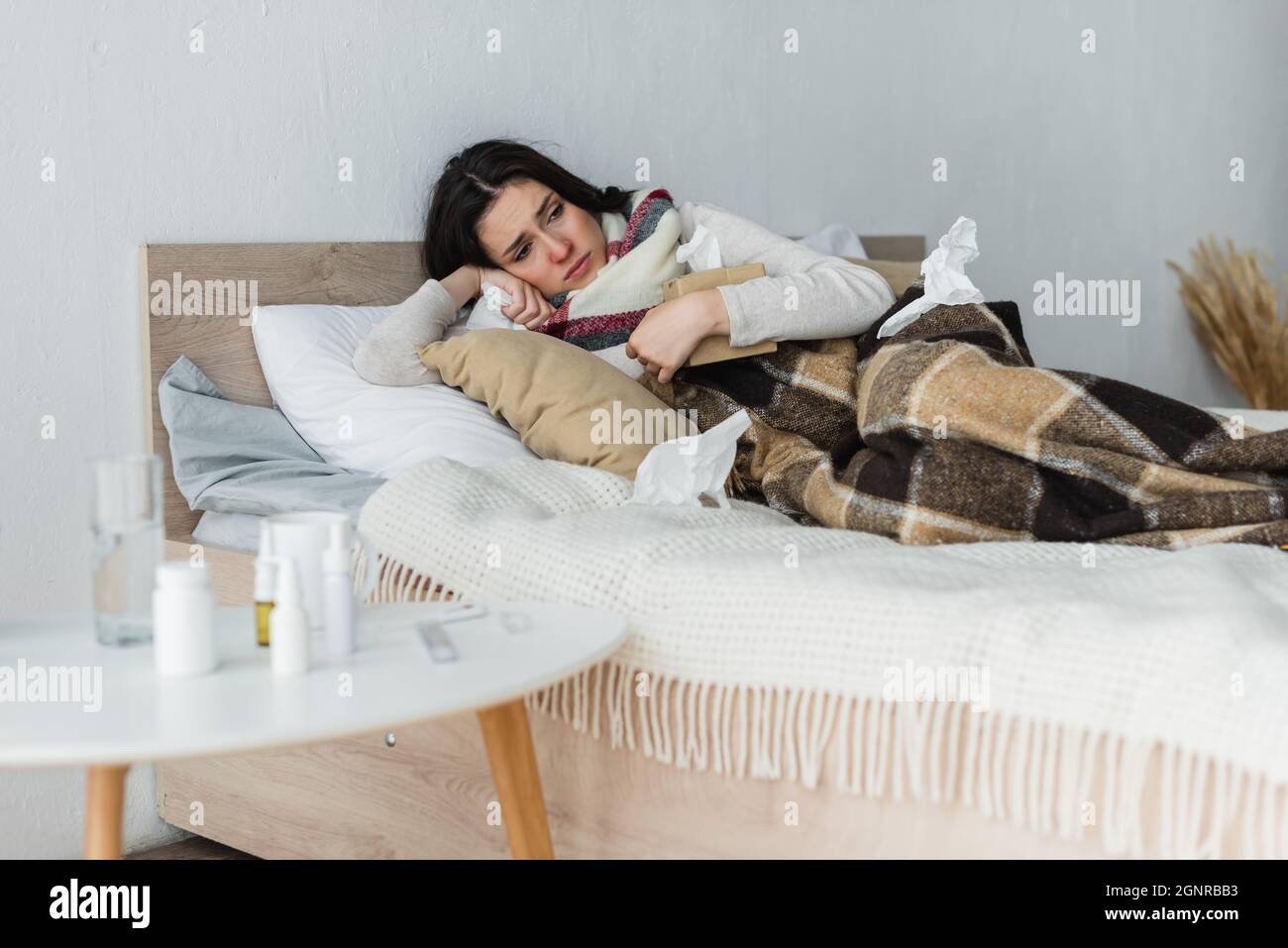 ill woman lying in bed under checkered blanket with pack of paper napkins Stock Photo