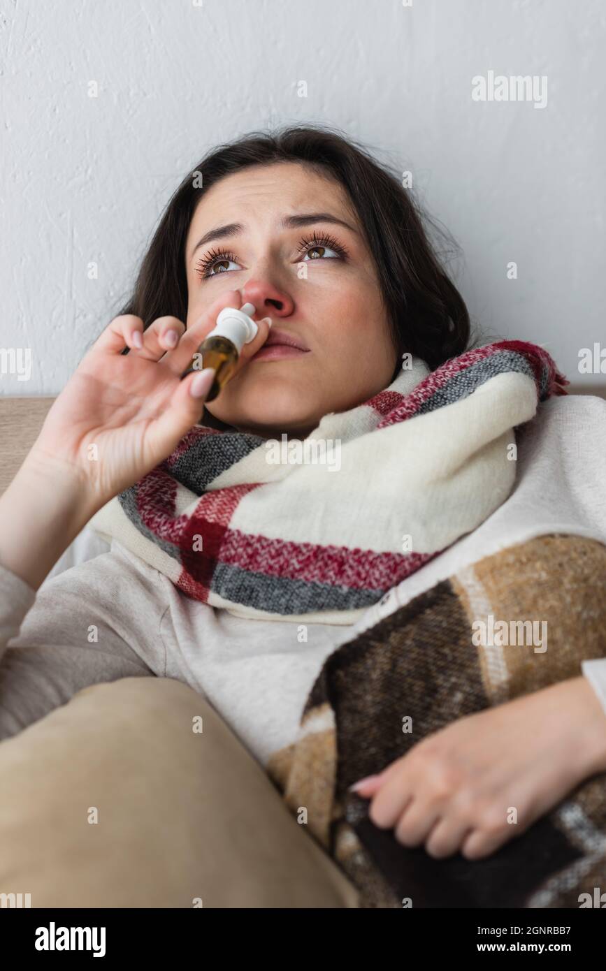 diseased woman in warm scarf using nasal spray in bed Stock Photo
