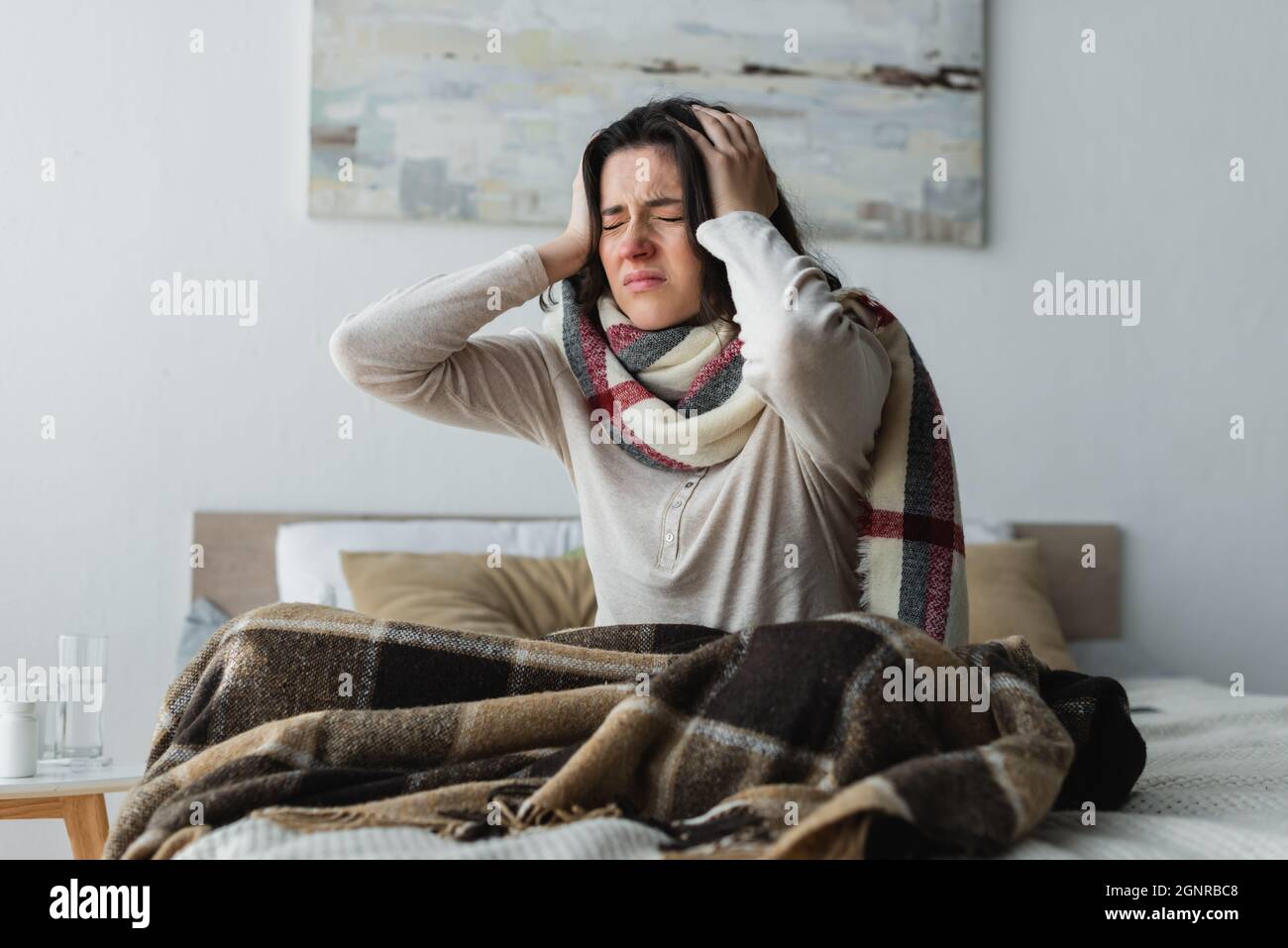 ill woman in warm scarf touching head while suffering from headache in bedroom Stock Photo